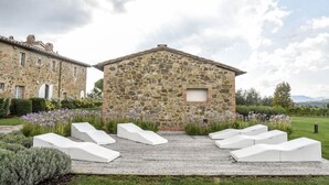 Un edificio de piedra con terraza de madera y sillones blancos.