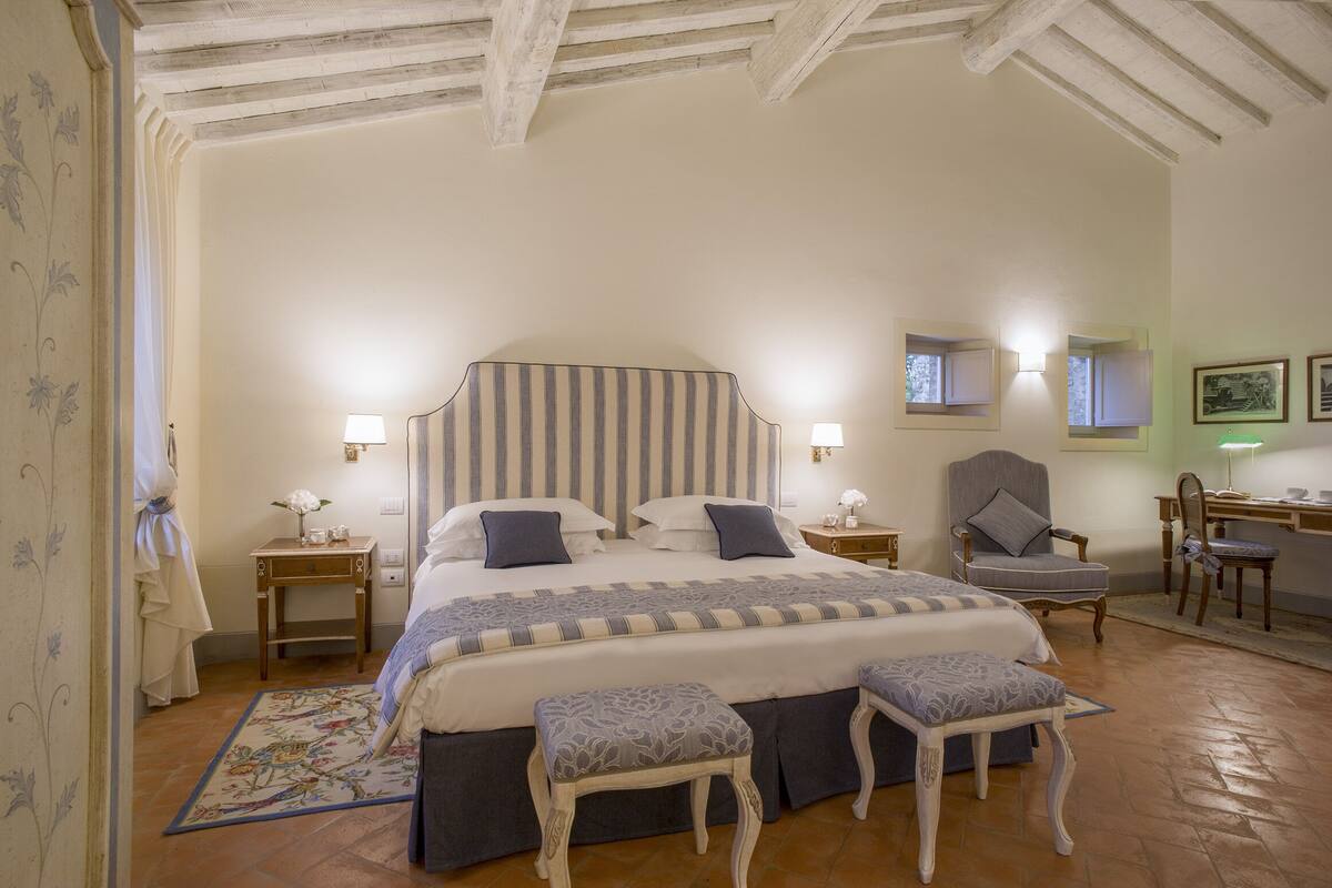 A bedroom with a large bed, two bedside tables, a chair, a desk, and a rug.