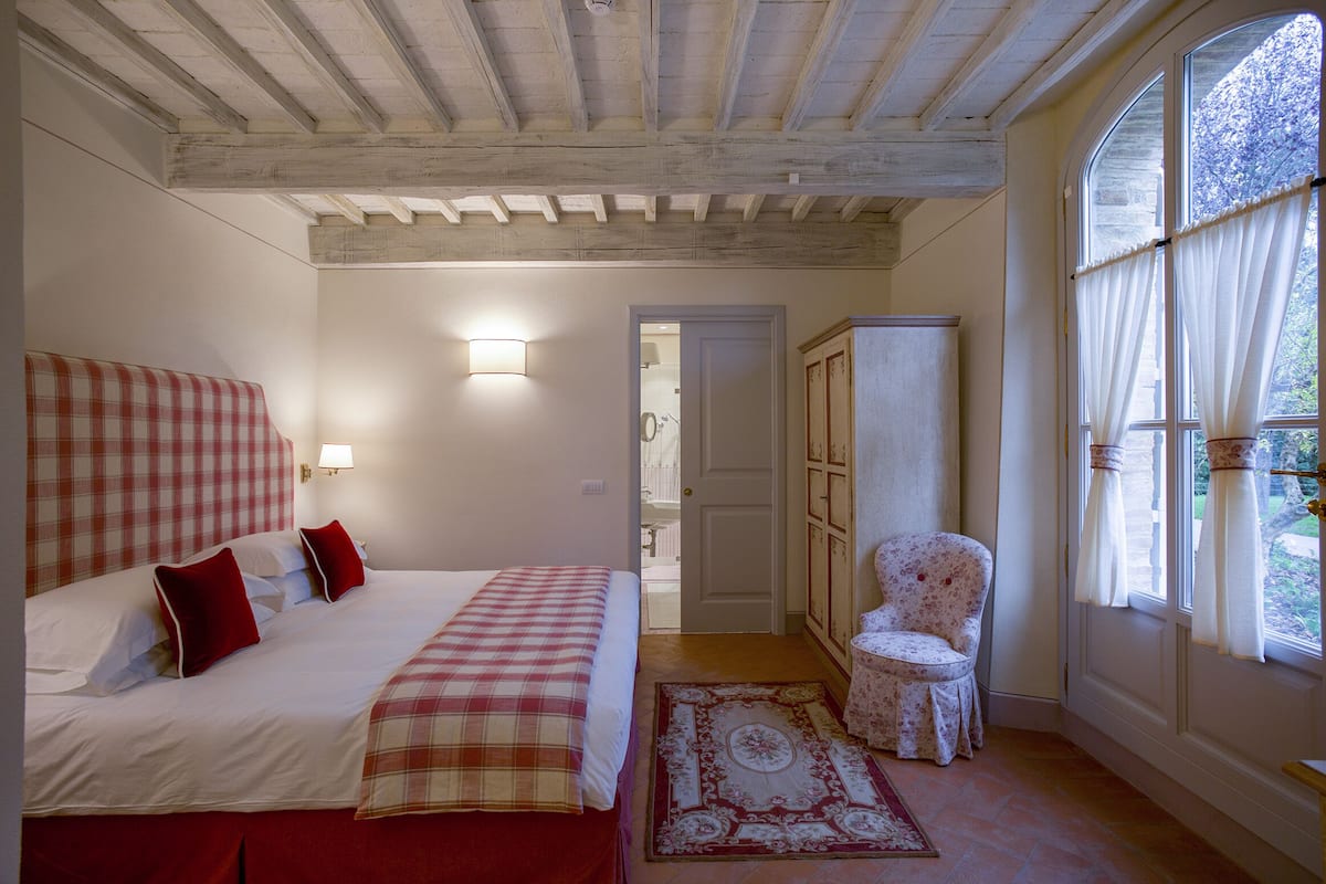 A bedroom with a bed, a chair, a wardrobe, and a window with curtains.