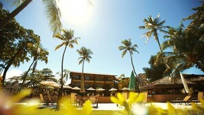 Un complexe hôtelier doté d’une piscine, de palmiers et d’un bâtiment au toit de chaume.
