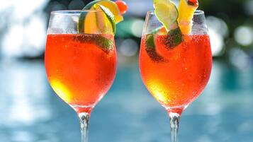 Zwei rote Cocktails mit Limette und Tomatenbeilage, platziert auf einem Tisch, im Hintergrund ein Pool.