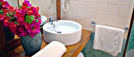 Un baño con un lavamanos redondo, un espejo, un teléfono, una toalla y un florero con flores.
