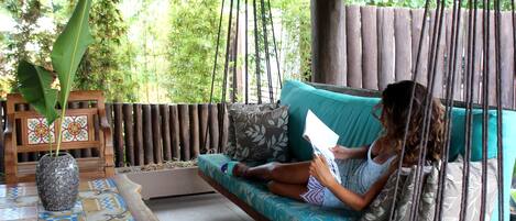 Une personne assise sur un canapé de style hamac, avec un coussin à motifs, est en train de lire un livre.