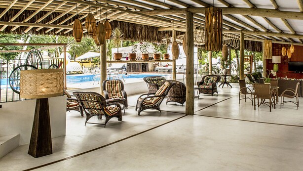 Un espacio al aire libre con techo, mobiliario de mimbre, piscina y bar.
