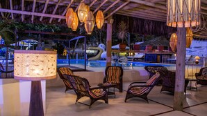 Zona junto a la piscina con sillas de mimbre, una lámpara grande y lámparas colgantes.