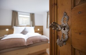 A bedroom with a wooden headboard, a bed with white linens, and a decorative metal handle on the door.