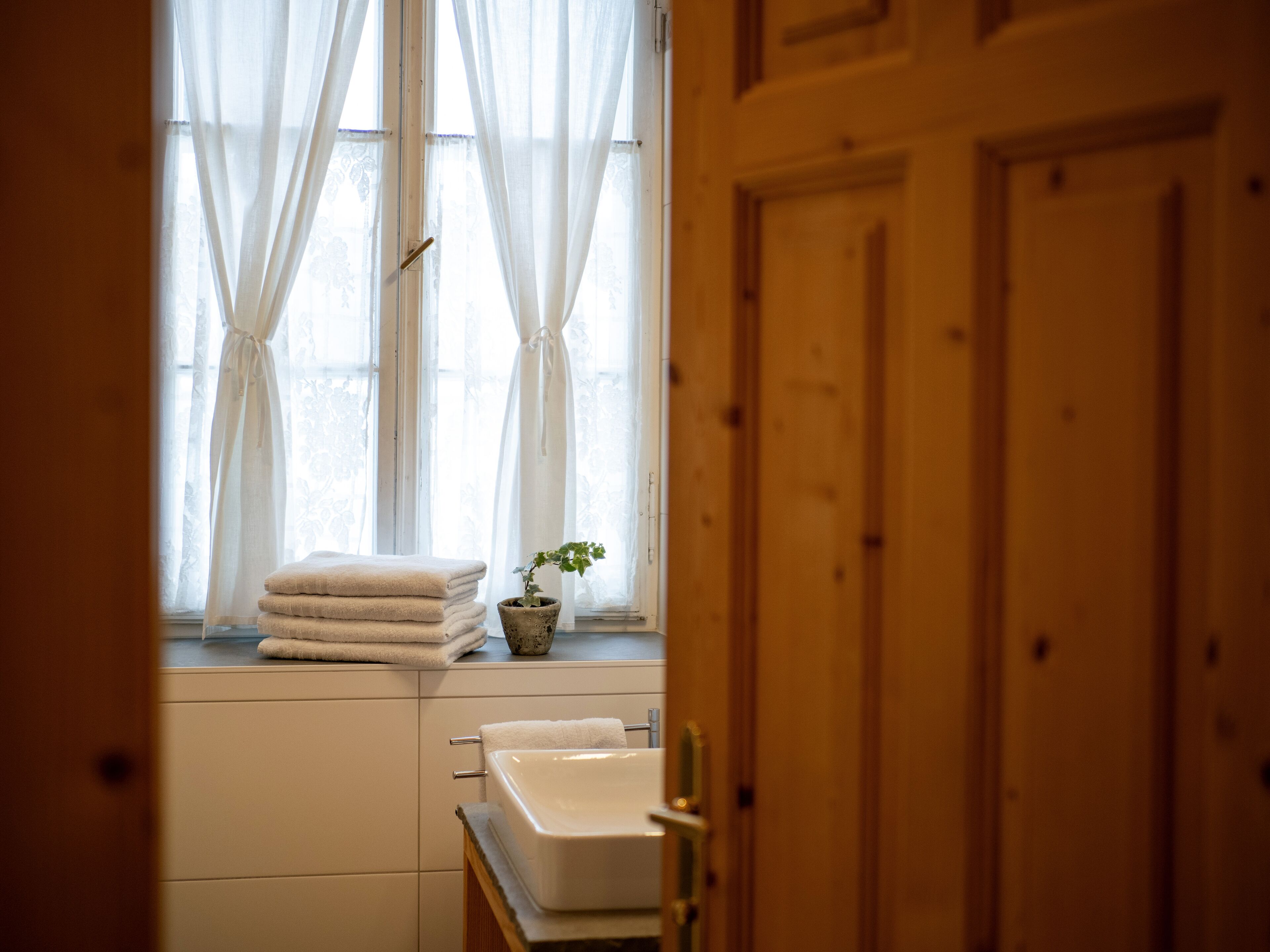 Un baño con ventana, un lavabo y una pila de toallas.