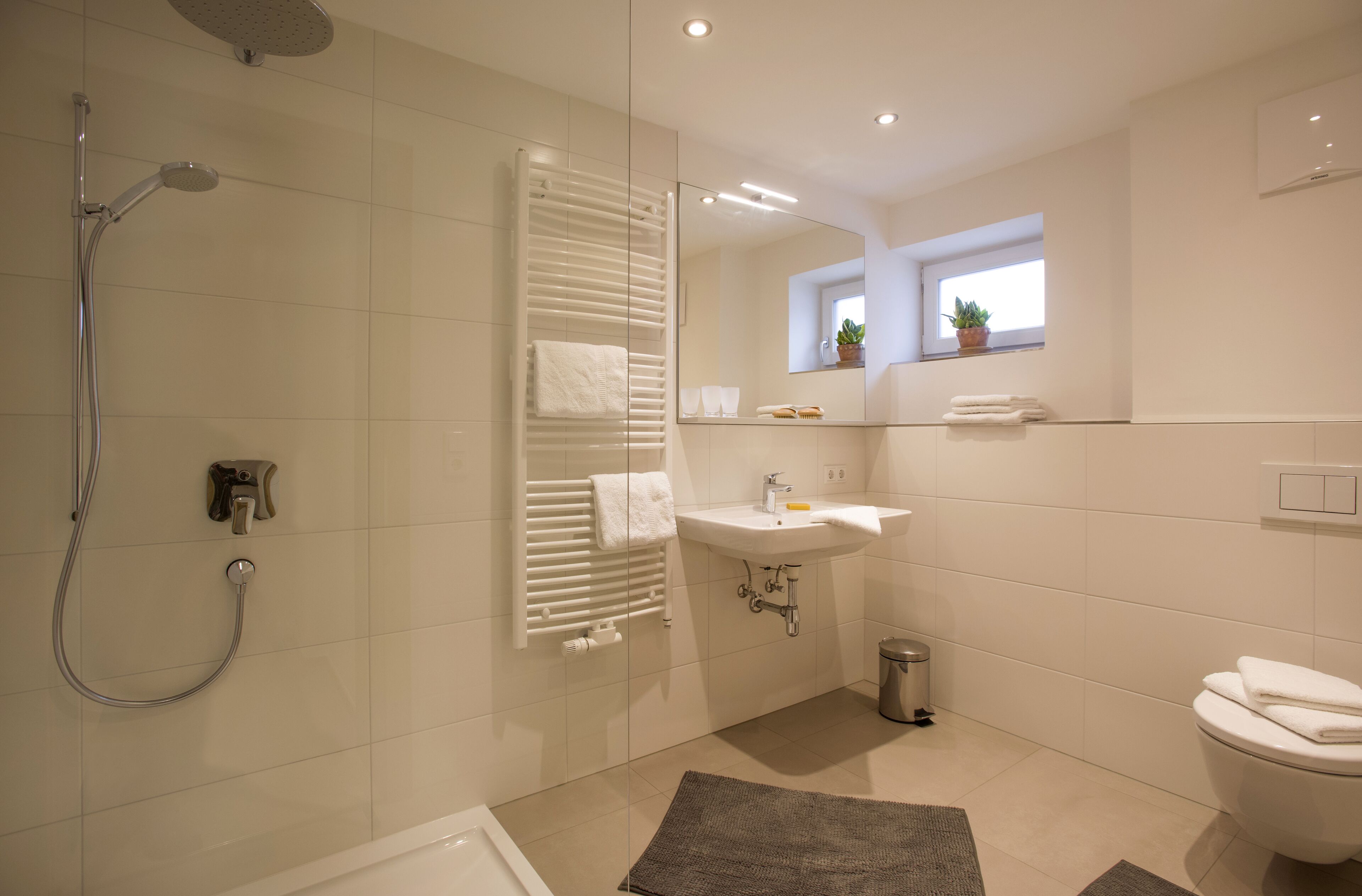 Ein modernes Badezimmer mit Dusche, Toilette, Waschbecken und einem Fenster mit Pflanzen.