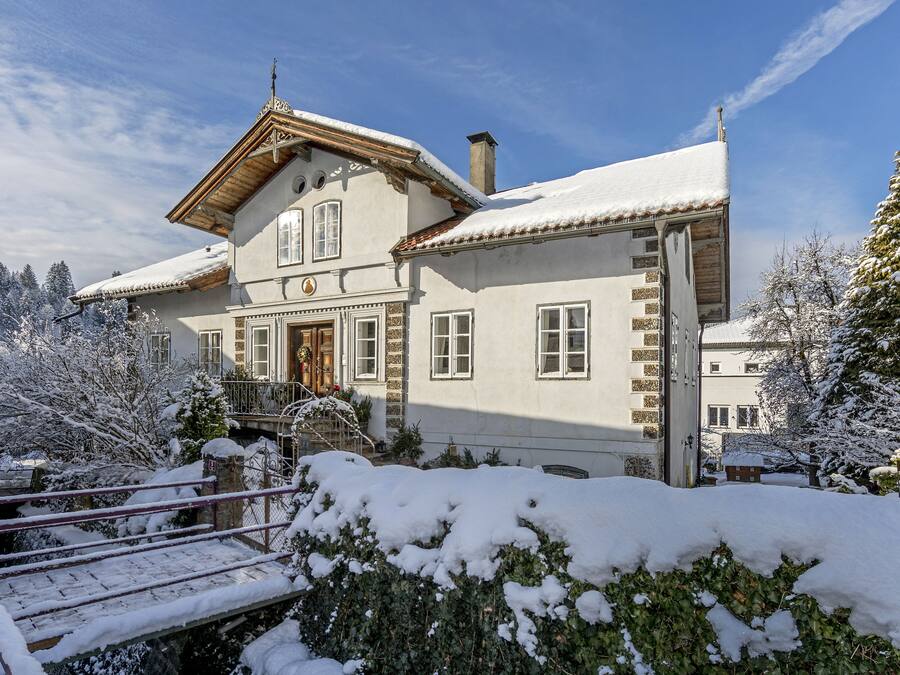 Een huis bedekt met sneeuw, met een houten gevel, een voordeur en een trap naar de ingang.