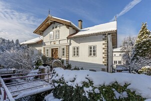 Una casa cubierta de nieve con fachada de madera, una puerta principal y una escalera que conduce a la entrada.