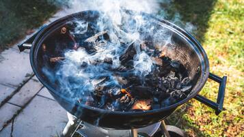 Ein tragbarer Grill mit sichtbarer Holzkohle und Rauch, auf einem Metallständer im Freien platziert.