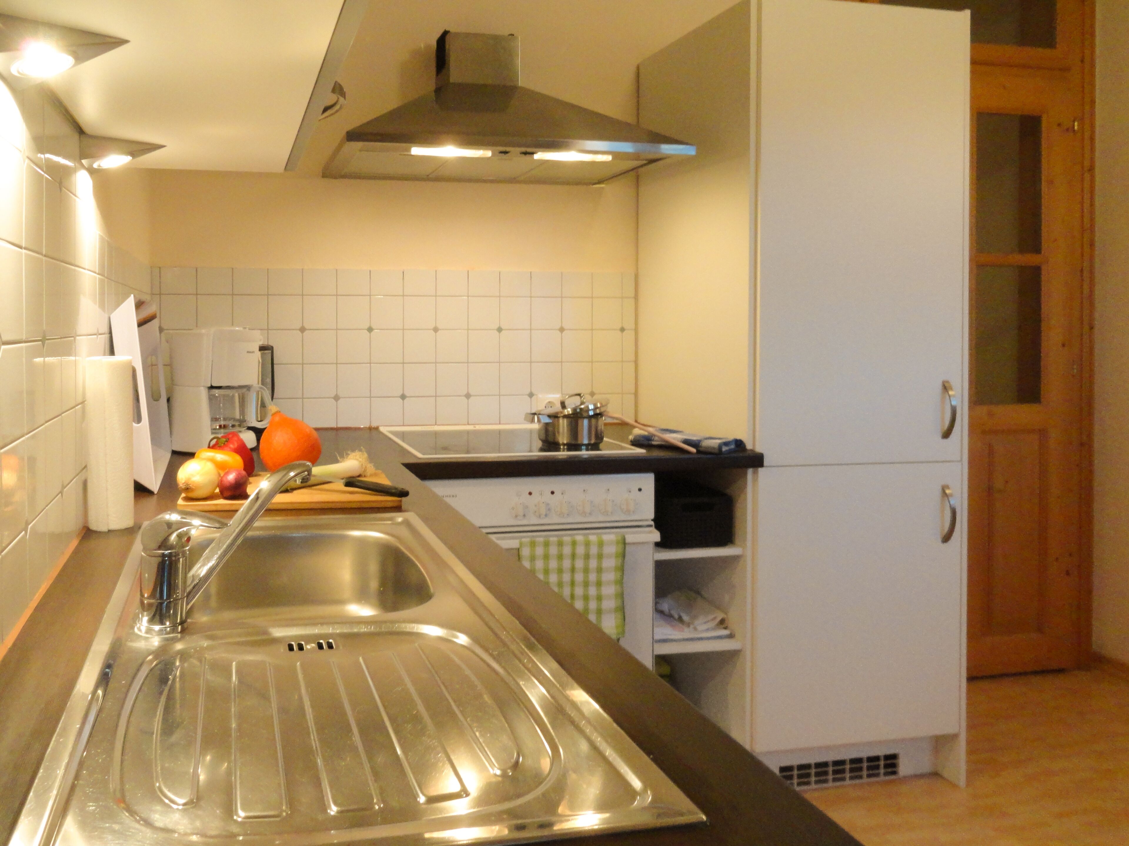 Una cucina moderna con lavello in acciaio inossidabile, mobili bianchi e una porta in legno.