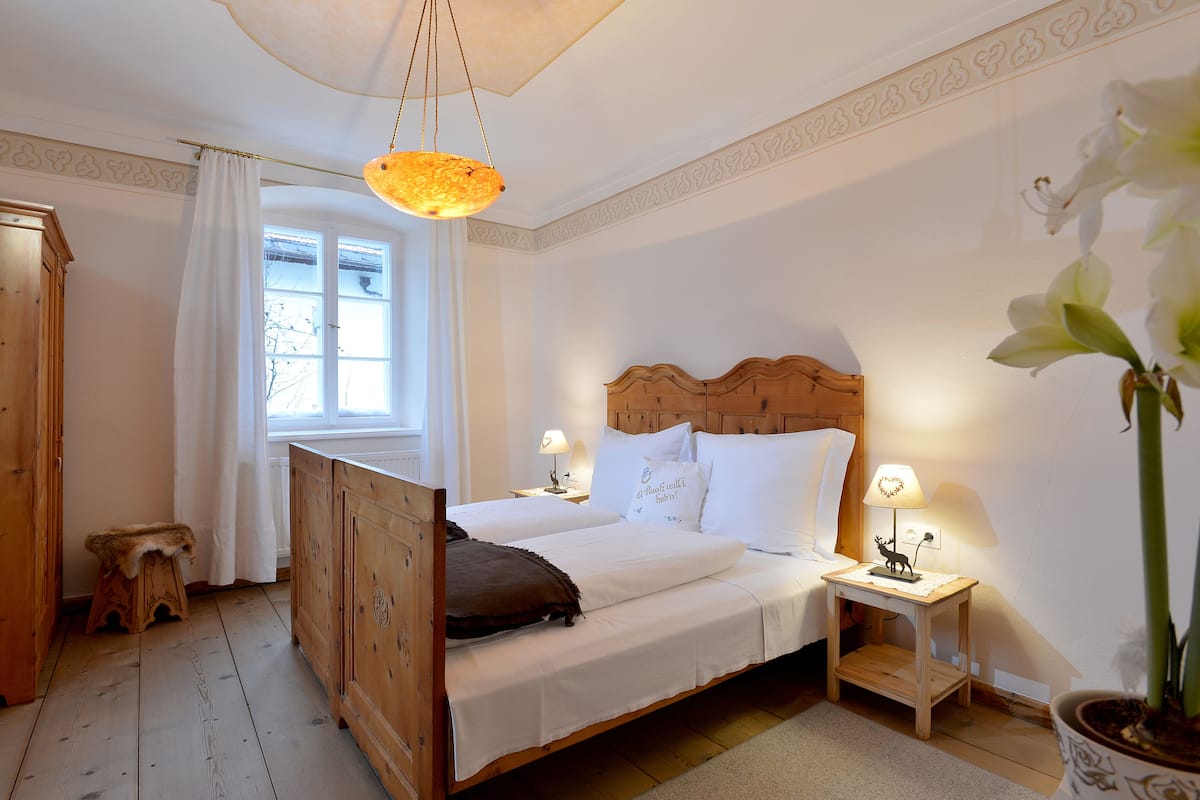 Une chambre à coucher avec un lit en bois, deux tables de chevet avec des lampes, une fenêtre avec des rideaux et une plante en pot.