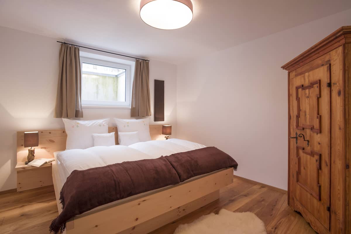 Une chambre à coucher avec un lit en bois, une table de chevet, une armoire et une fenêtre avec des rideaux.