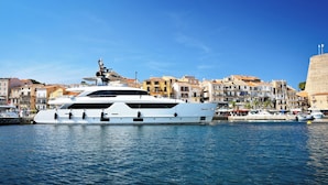 A large white yacht docked at a marina with a backdrop of colorful buildings and a clear blue sky. - Camping International (Calvi)