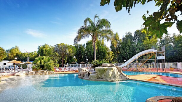 A swimming pool with a slide, lounge chairs, and palm trees. - Camping International (Calvi)