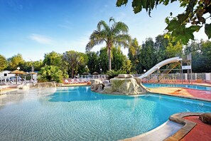 Une piscine avec un toboggan, des chaises longues et des palmiers.