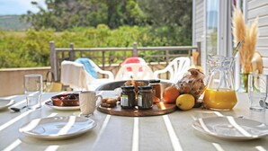 A breakfast table with plates, glasses, and food items on a balcony overlooking greenery. - Camping International (Calvi)