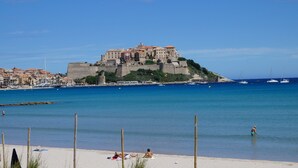 A coastal town with a prominent castle on a hill, a sandy beach, and calm waters. - Camping International (Calvi)