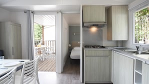 A compact kitchen with a central island, a dining area with a table and chairs, and a bedroom with a bed and nightstand. - Camping International (Calvi)