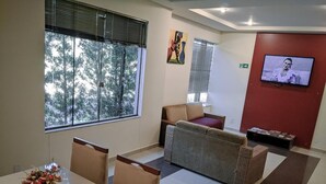 A modern waiting area with a dining table, chairs, a sofa, and a television. - Rede Andrade Biton (Foz do Iguaçu)