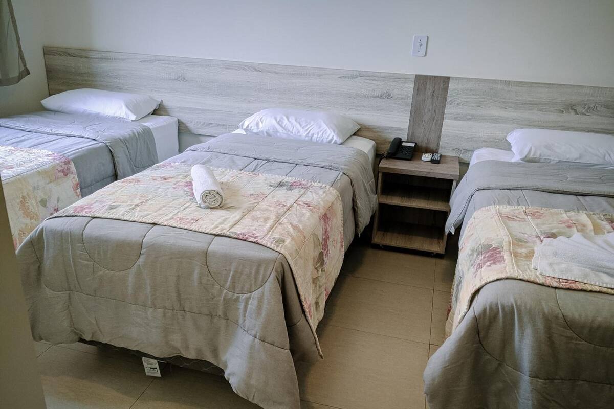 Habitación de hotel con tres camas dispuestas en fila, cada una con cabecero de madera y ropa de cama floral.