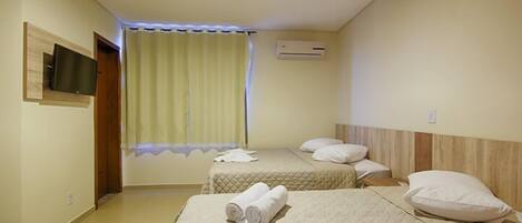A hotel room with two beds, a flat-screen TV mounted on the wall, an air conditioning unit, and a window with curtains.