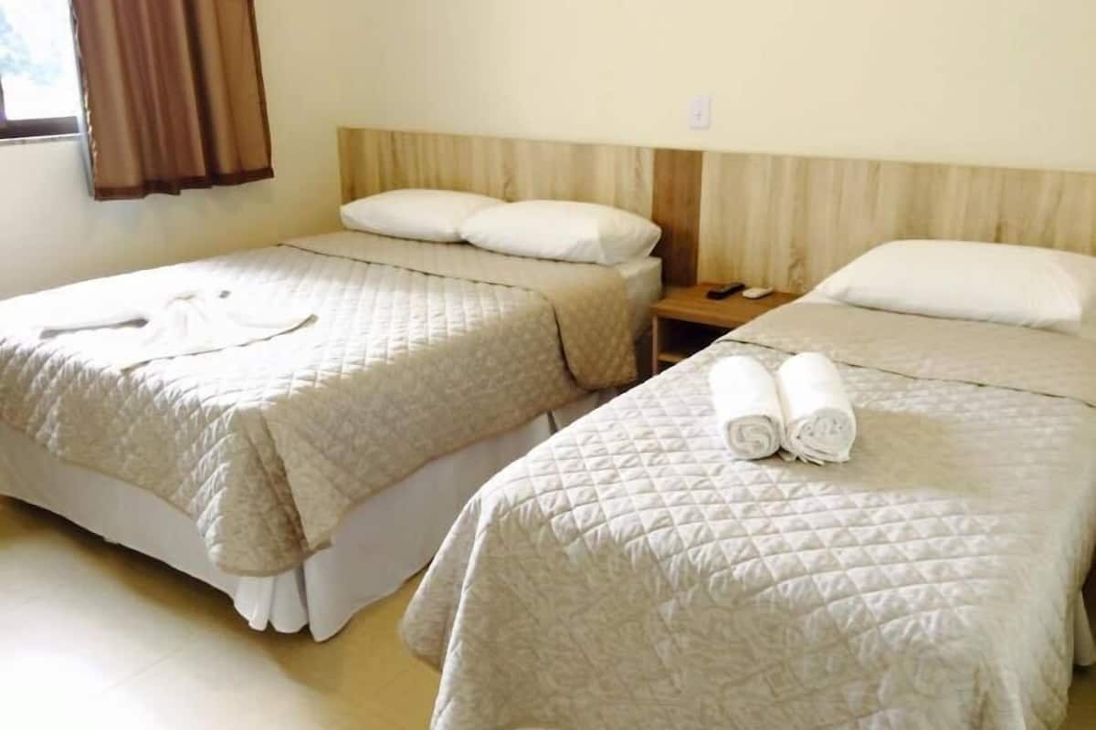 Dos camas individuales con ropa de cama y almohadas color beige, un cabecero de madera y una mesita de noche con un control remoto.
