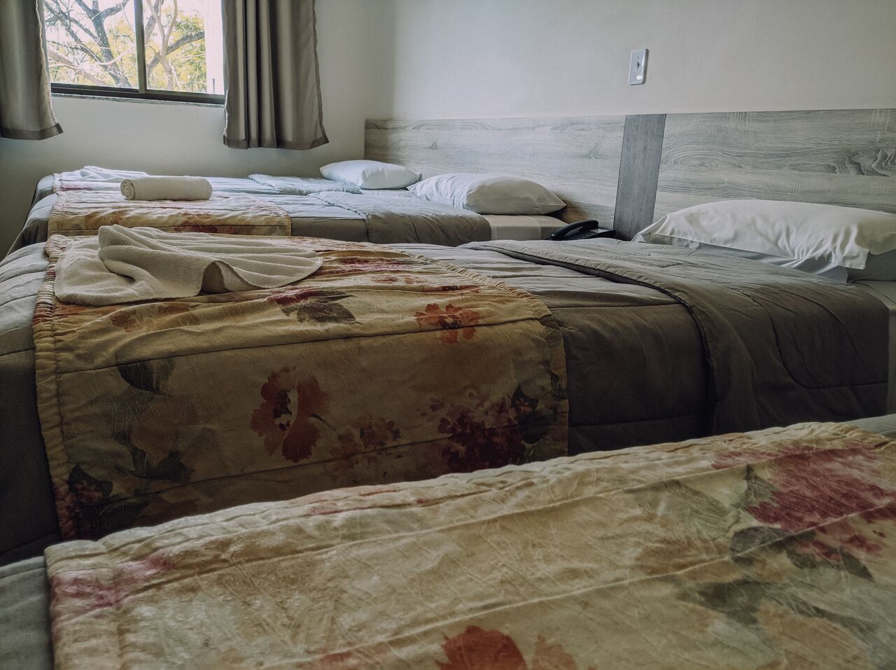 A hotel room with two beds, a window with curtains, and a wooden headboard.