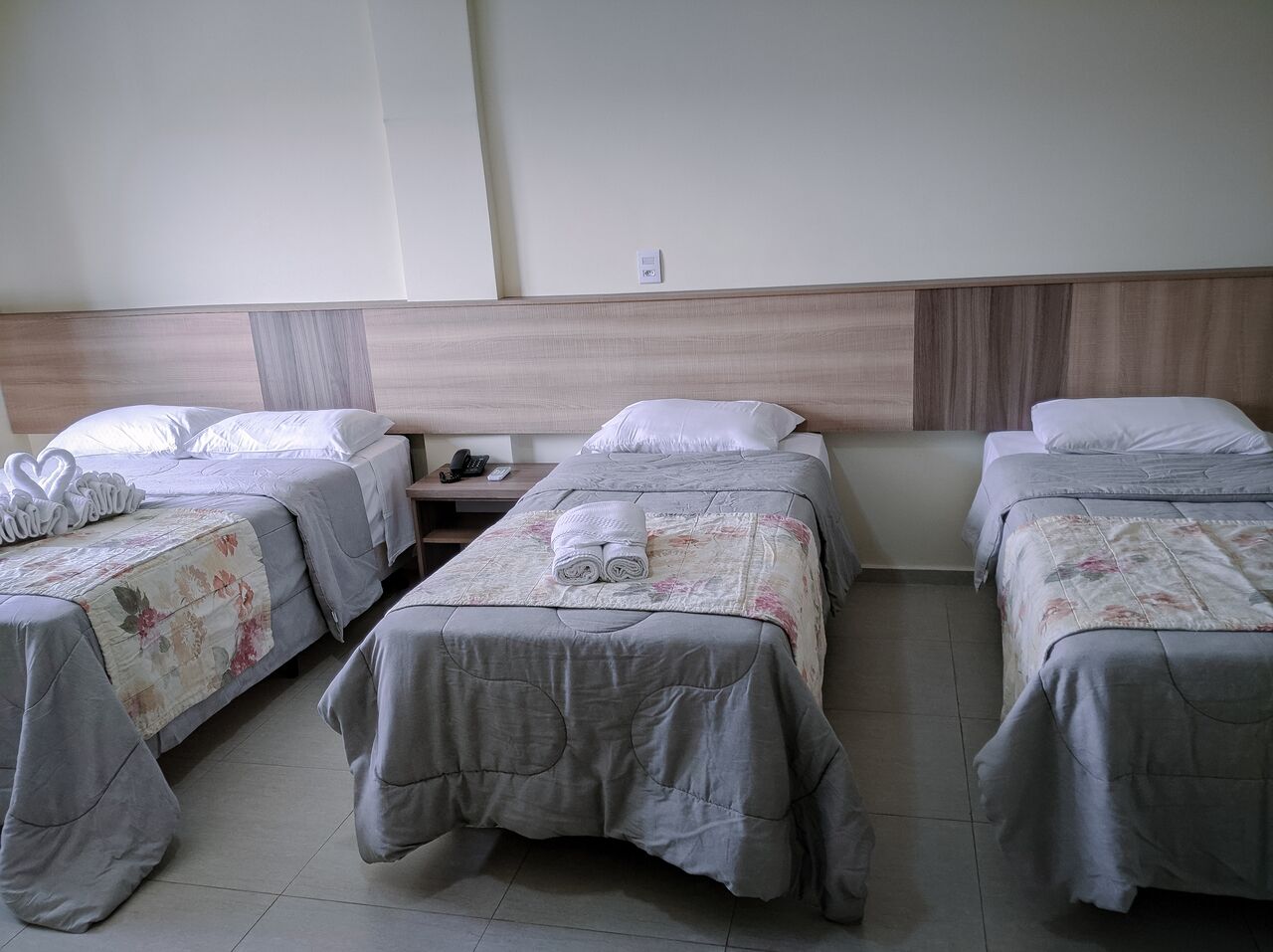 Habitación de hotel con tres camas individuales, cada una con colcha de estampado floral y almohada blanca. La habitación tiene cabecera de madera y piso de baldosas.
