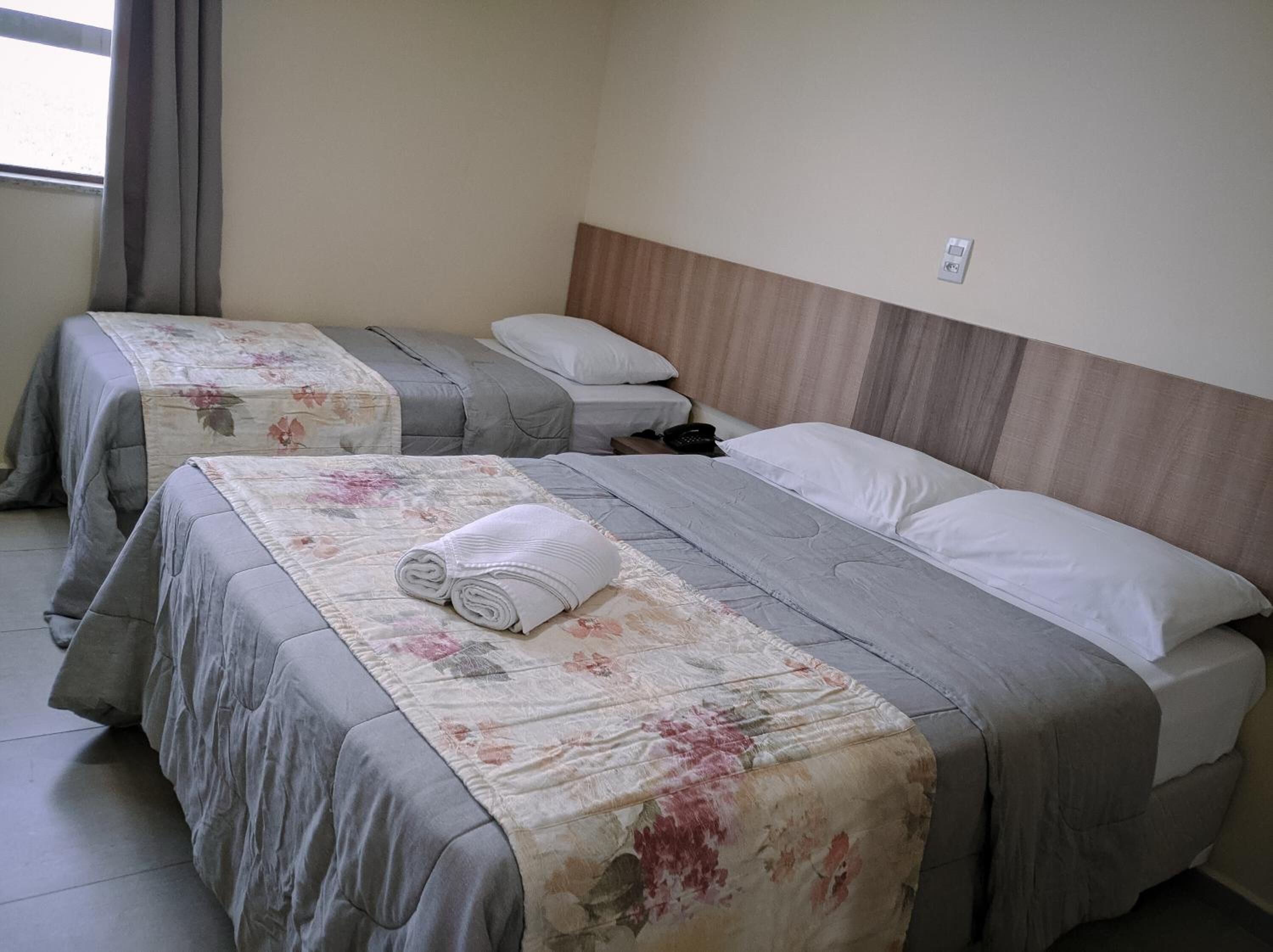 Une chambre d’hôtel avec deux lits, chacun agrémenté de draps à motifs floraux et une serviette roulée posée sur l’un des lits.