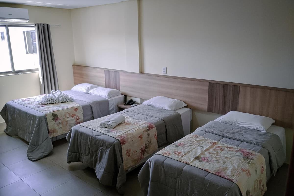 Habitación de hotel con tres camas individuales, cada una con una colcha estampada y toallas enrolladas.