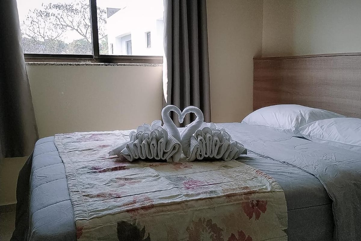Una habitación de hotel con una cama, un ventanal con cortinas y una pared con paneles de madera.