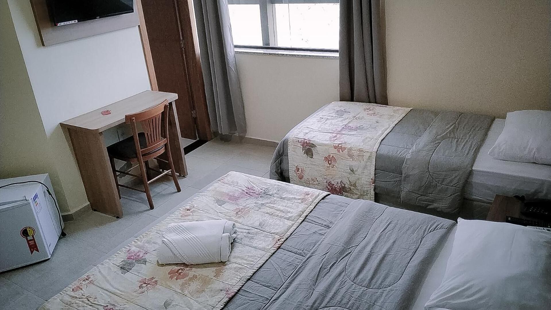 Habitación de hotel con dos camas, un escritorio, una silla y un televisor montado en la pared.