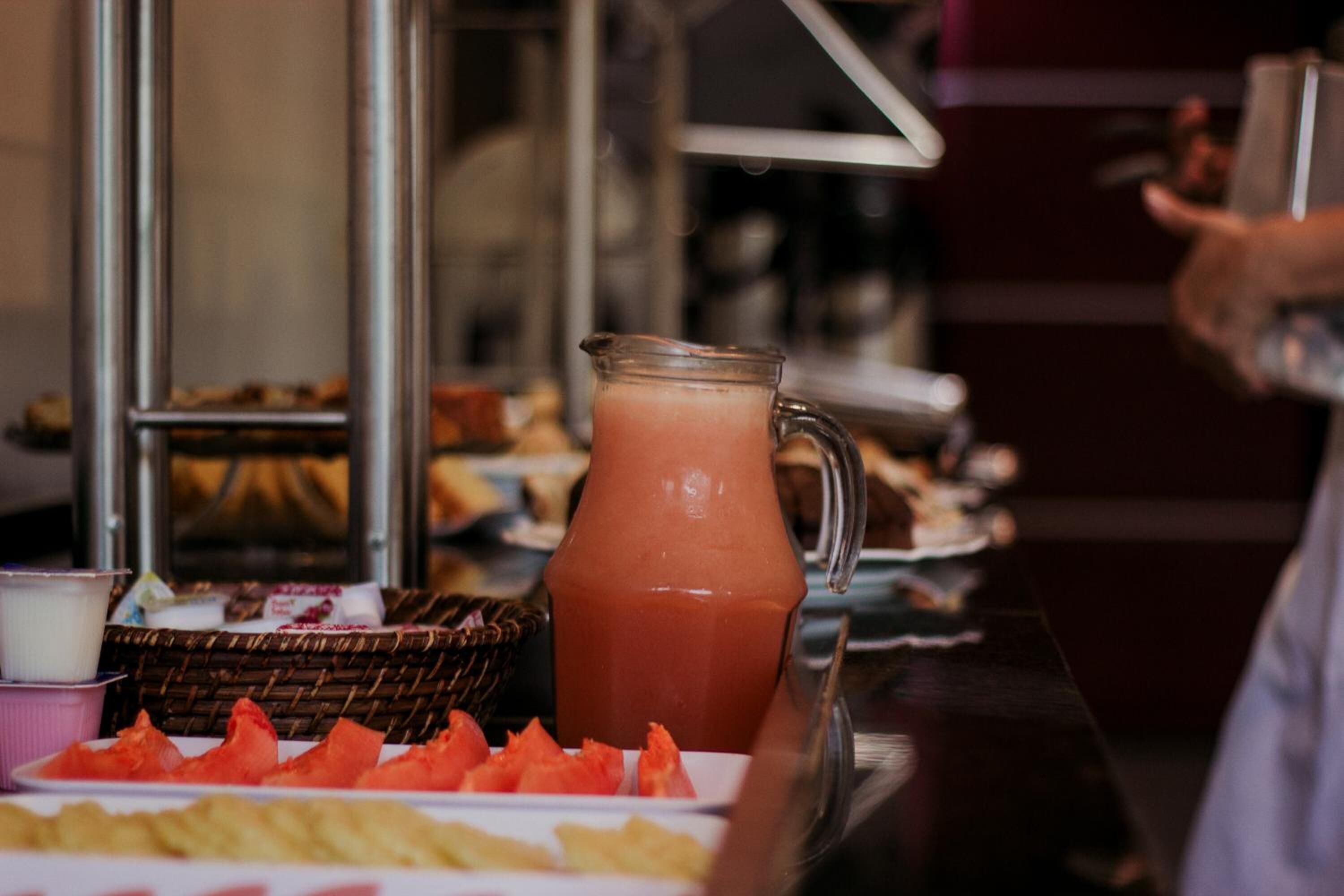 Un buffet avec une carafe de boisson rose, des tranches de pastèque et divers plats.