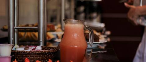 Un buffet avec une carafe de boisson rose, des tranches de pastèque et divers plats.