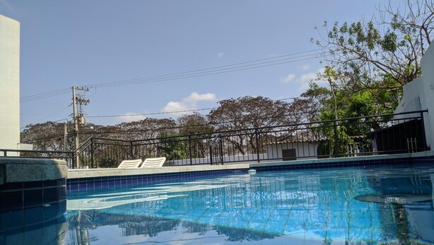 A swimming pool with clear blue water, surrounded by a metal fence and trees. - Rede Andrade Biton (Foz do Iguaçu)