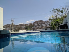 A swimming pool with clear blue water, surrounded by a metal fence and trees.