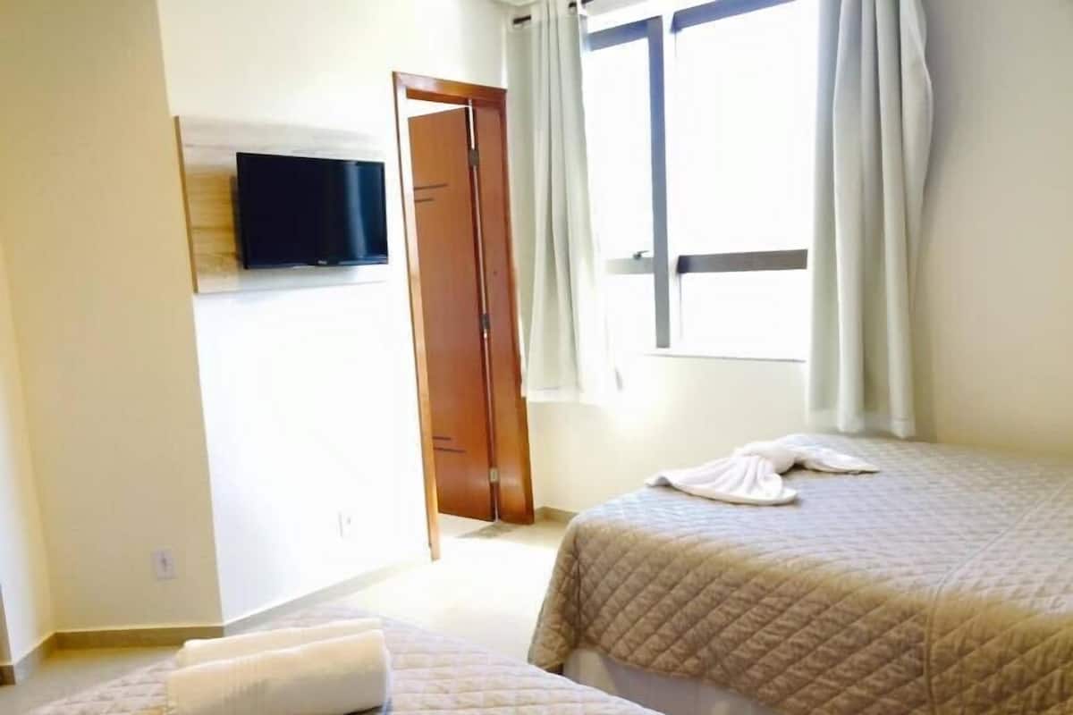 Una habitación de hotel con dos camas, un televisor en la pared y una ventana con cortinas.