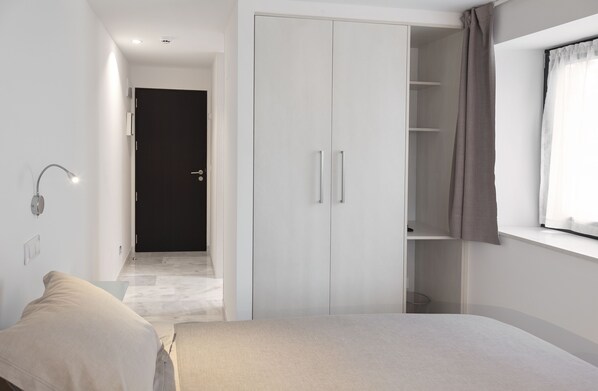 A bedroom with a bed, a wardrobe, a bedside table, and a window with curtains.