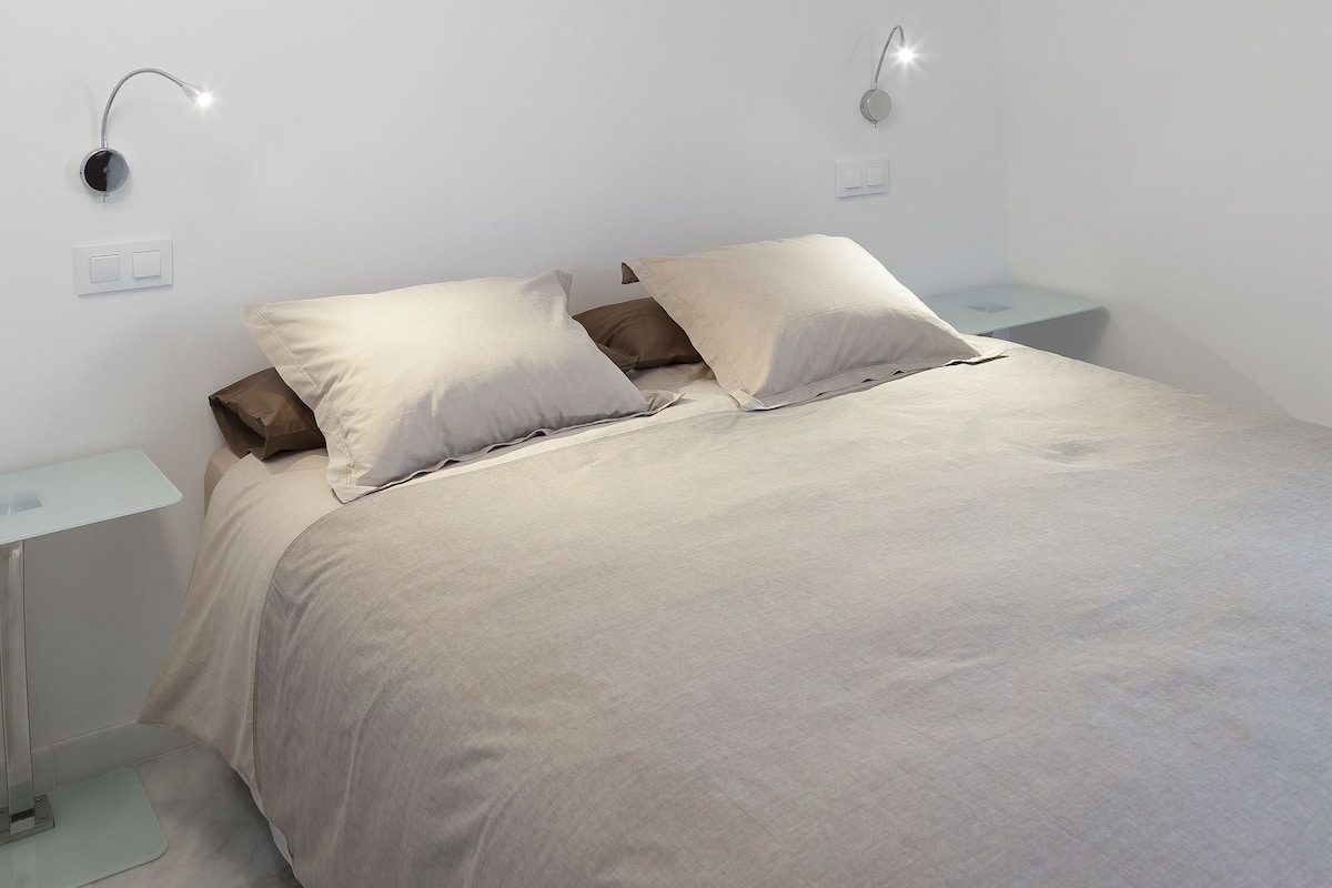 A bedroom with a bed, bedside tables, and wall-mounted lighting.