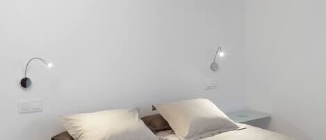 A bedroom with a bed, bedside tables, and wall-mounted lighting.