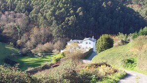 A house with a sloped roof, surrounded by a lush green landscape and dense forest. - Finca Portizuelo (Valdes)