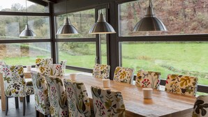 A dining area with a wooden table and floral-patterned chairs, large windows with a view of a grassy landscape, and pendant lighting. - Finca Portizuelo (Valdes)