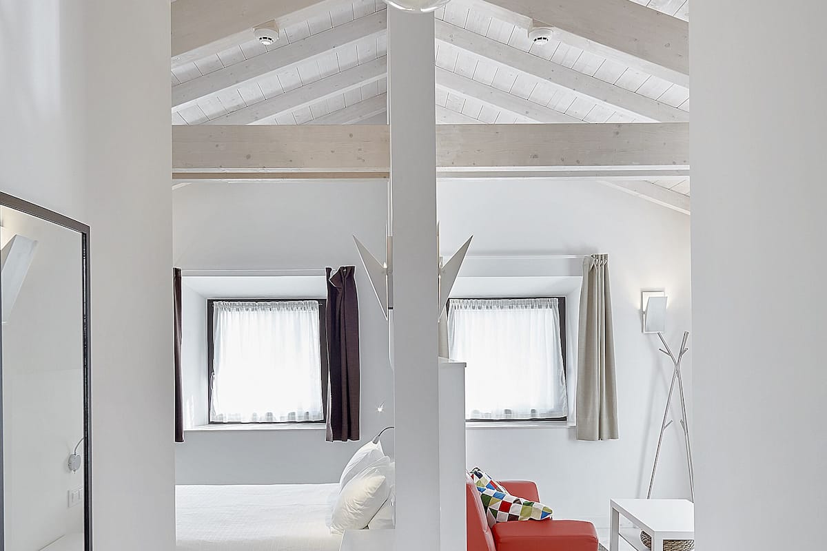 A modern bedroom with a large bed, a red chair, and a white desk.
