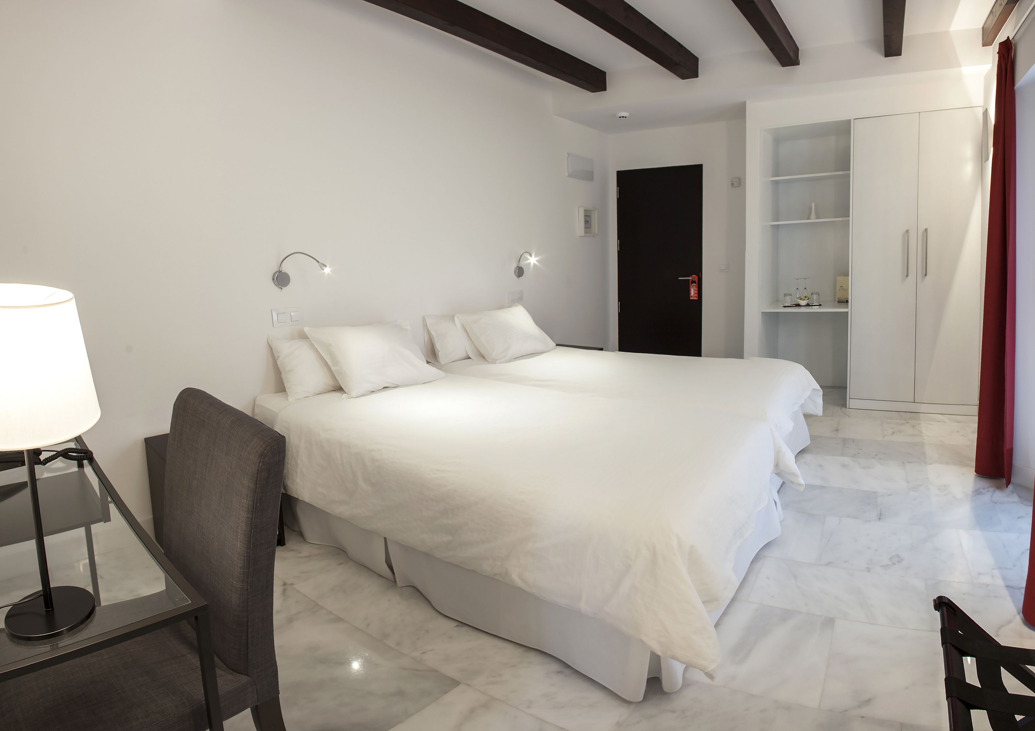 A modern hotel room with a large bed, a desk with a lamp, and a wardrobe.