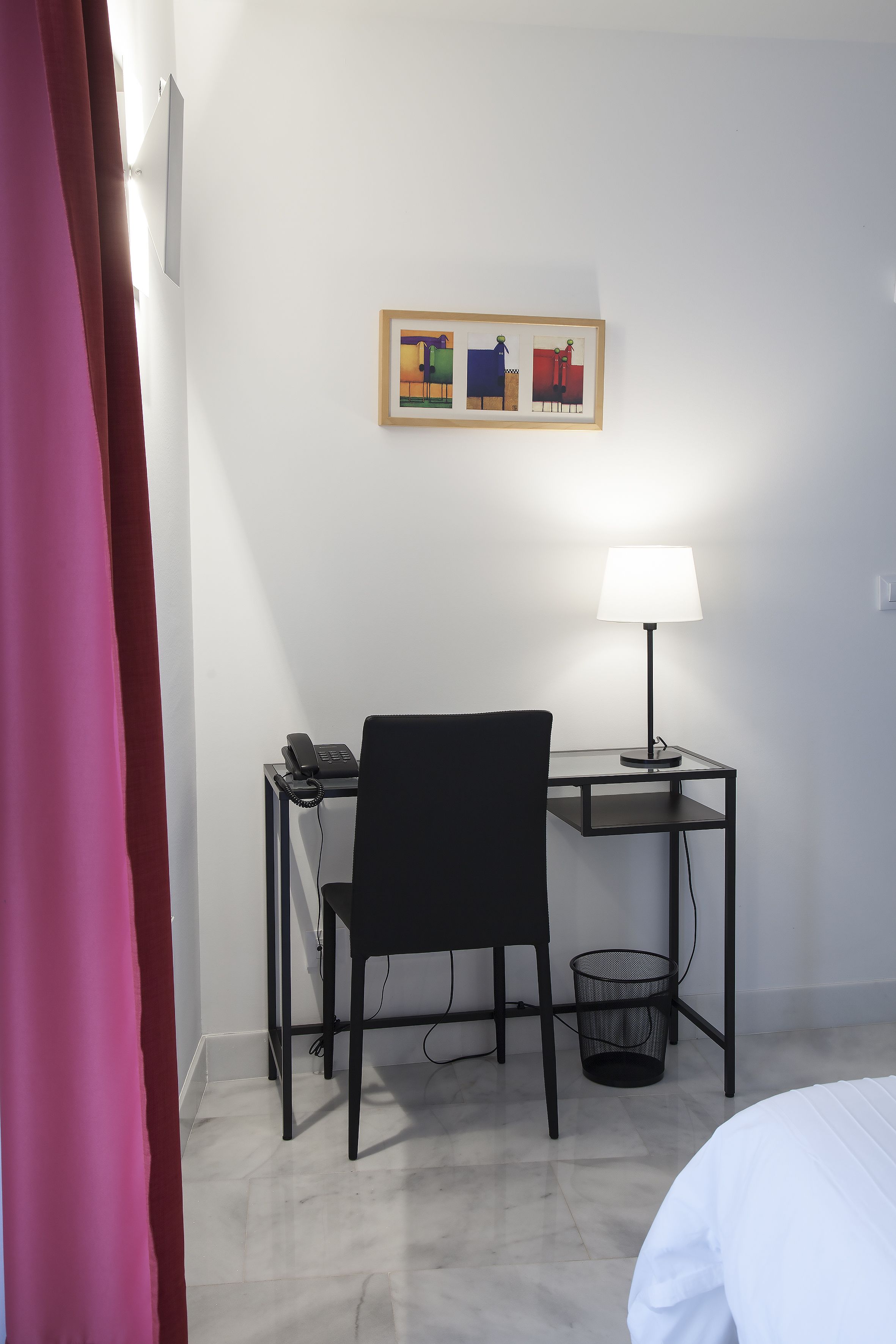 Habitación de hotel con escritorio, silla, lámpara y un cuadro en la pared.
