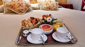 A breakfast tray with bread, a grapefruit, juice, and cups on a bed. - Ca Princess (Venice)
