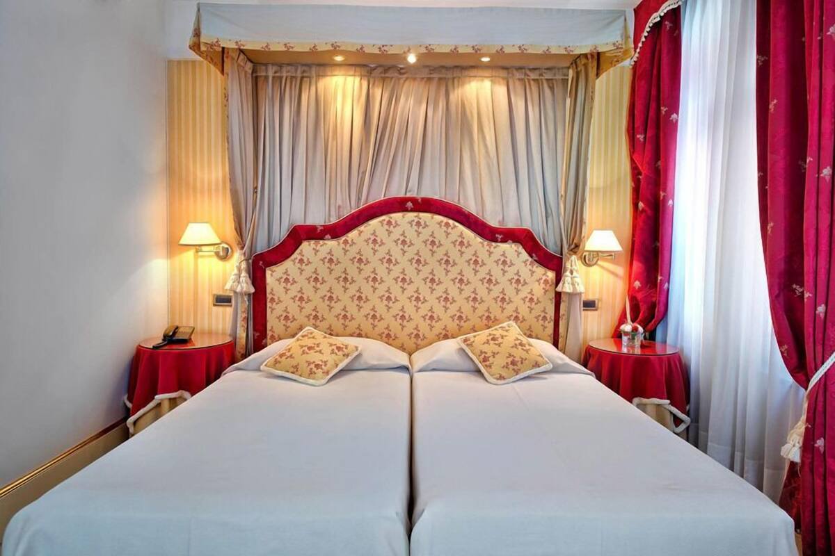 Un lit double avec une tête de lit à motifs floraux, deux tables de chevet avec des lampes et des rideaux rouges.