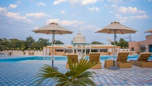 A pool area with lounge chairs and umbrellas, a small pavilion, and a clear sky. - Pratap Mahal, Ajmer - IHCL SeleQtions (Pushkar)